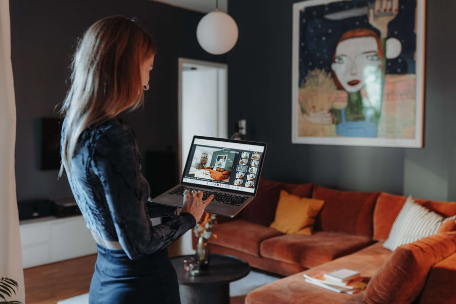 Kundin zeigt auf dem Laptop ihr Online-Interior-Design-Konzept im fertig eingerichteten Wohnzimmer mit Samtsofa