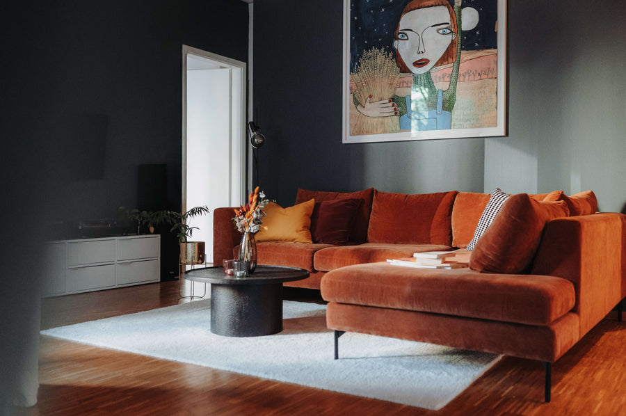 Fertiges Wohnzimmer aus einem Schöner*INNEN-Projekt: rostrotes Samtsofa, dunkle Wand, großes Kunstwerk und runder Couchtisch