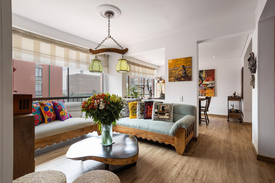 Eclectic Style: Wohnzimmer mit Vintage-Holzsofa, bunt bestickten Kissen, Gemälden, Pendelleuchte mit Rosette und Blumenstrauß