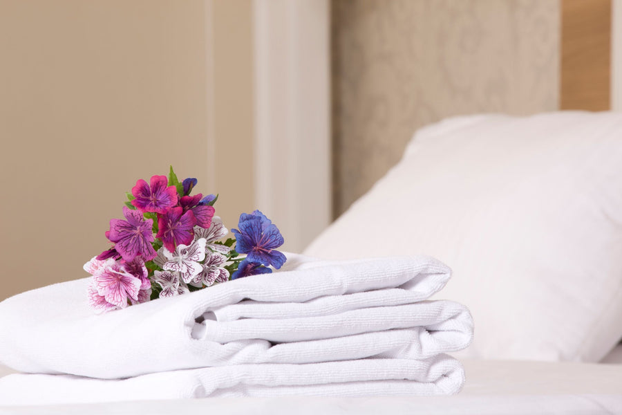 Frisch bezogenes Gästebett mit gefalteten weißen Handtüchern und kleinem Blumenstrauß als Willkommensgruß in der Ferienwohnung