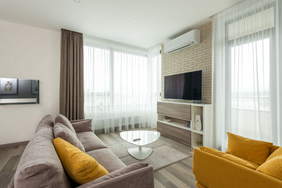 Wohnzimmer mit harmonischem Farbkonzept aus Taupe, Weiß und Senfgelb – Sofa, Sessel und Kissen greifen die Akzentfarbe auf