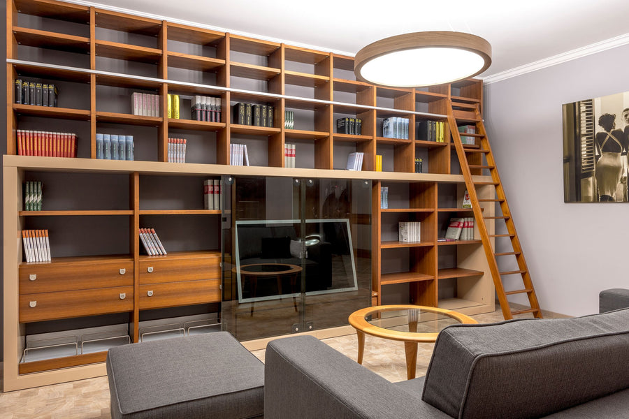 Hohe Decken einrichten: deckenhohes Holzregal mit Bibliotheksleiter, große Pendelleuchte und graues Sofa im Wohnzimmer