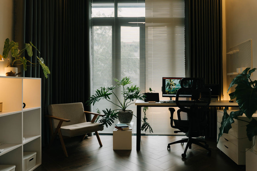 Wohnliches Home Office mit Schreibtisch vor großem Fenster, Sessel, Regal und großen Grünpflanzen im Tageslicht