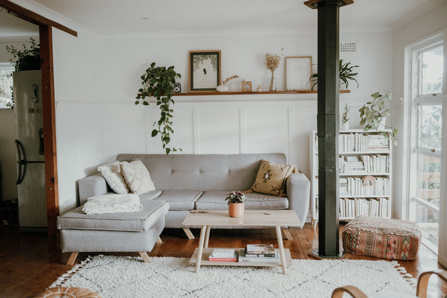 Skandinavischer Einrichtungsstil: helles Wohnzimmer mit grauem Sofa, Holztisch, Berber-Teppich, Wandregal und Pflanzen