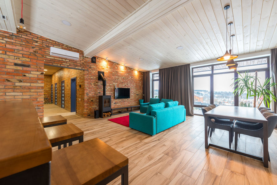 Urban Industrial Style: offener Wohnraum mit Backsteinwand, Holzdecke, Kaminofen, türkisem Sofa und großen Fensterfronten